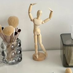 a wooden mannequin holding several makeup brushes in it's hand next to a glass container