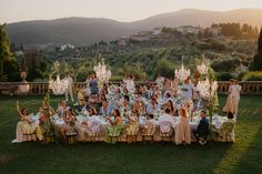 a large group of people sitting around a dinner table in the middle of a field