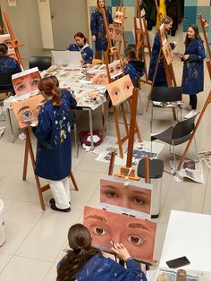 a group of people standing around with paintings on easels in the middle of a room