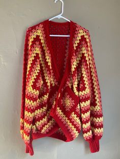 a red and yellow crocheted sweater hanging on a white wall next to a hanger