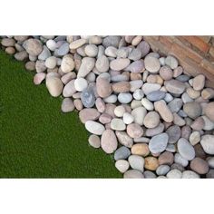 there is a pile of rocks next to a brick wall and green grass in the background