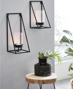 two black metal wall sconces with candle holders on them next to a potted plant