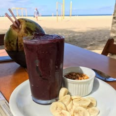 a smoothie and banana slices on a plate at a beach side restaurant with people in the background