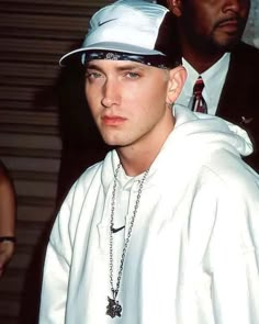 a young man wearing a white hat and chain around his neck is looking at the camera