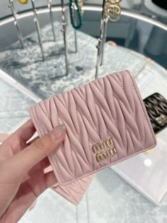 a hand holding a pink wallet in front of a display case with jewelry on it