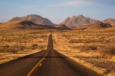 an empty road in the middle of nowhere, with mountains in the backgroud