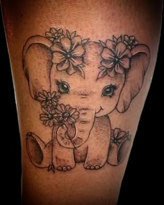 an elephant with flowers on it's head is sitting next to a woman's leg