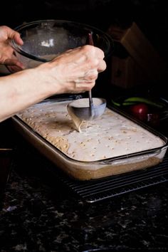 a person holding a spoon over a pan with food on it