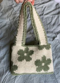 a hand holding a crocheted purse on top of a bed