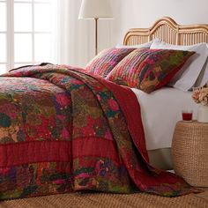 a bed with red and green quilts on it next to a wicker basket