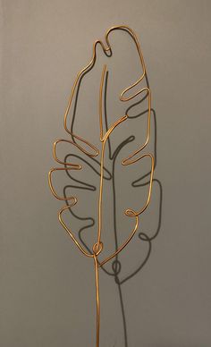 a metal sculpture with a leaf on it's side, in front of a gray wall