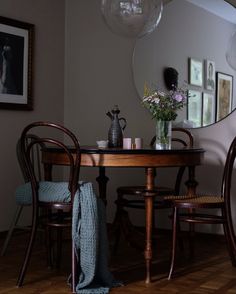 a dining room table with chairs and a round mirror on the wall next to it