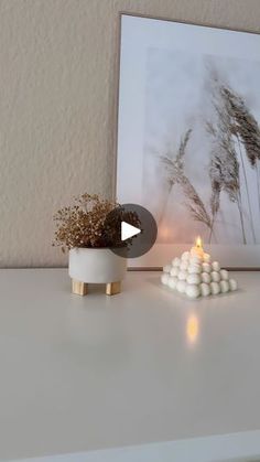 a white table topped with a vase filled with flowers and marshmallows next to a lit candle