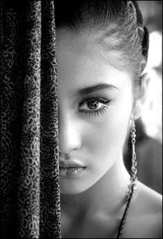 a woman with green eyes and purple lipstick looks out from behind the curtain in black and white