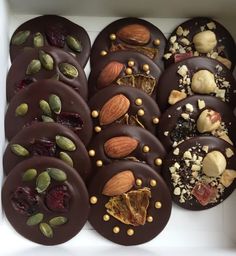 a box filled with chocolate covered donuts topped with nuts and dried fruit toppings