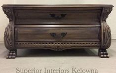 a wooden dresser with two drawers and ornate carvings on the bottom drawer, sitting against a white wall