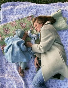 a woman laying on top of a blanket next to a baby