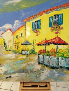 an oil painting of a yellow building with blue shutters and red umbrellas in front of it