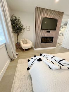 a white bed with black and white blankets on it in front of a tv mounted to the wall