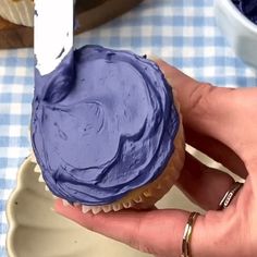 a cupcake with blue frosting being held by someone's hand in front of it