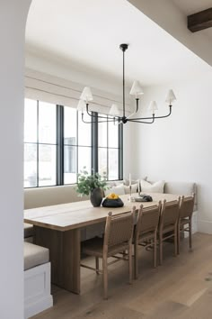 a dining room table with chairs and a bench in front of large windows that look out onto the street