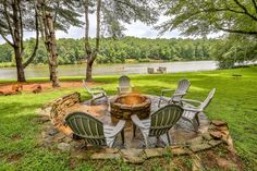 a fire pit with chairs around it in the middle of some grass and trees near water