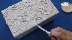 someone is working on an intricately designed box with white paint and a cup of coffee in the background