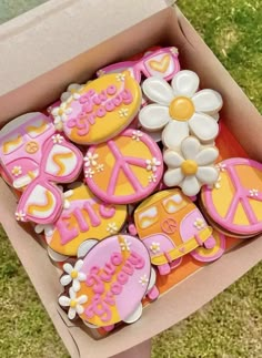 a box filled with decorated cookies sitting on top of a grass covered field next to a white flower