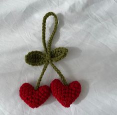 two crocheted hearts hanging from a green cord on a white sheet with the string attached to them