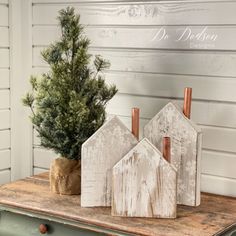 three wooden houses sitting on top of a table next to a small tree in a pot