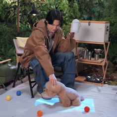 a man kneeling down next to a teddy bear on top of a blue cloth covered ground