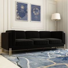 a black couch sitting in front of a blue rug on top of a wooden floor