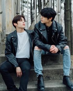 two young men sitting on the steps in front of a building, one is wearing a black leather jacket and the other wears a white t - shirt