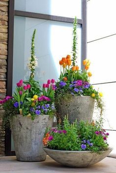 three cement planters filled with colorful flowers sitting on the side of a building next to a window