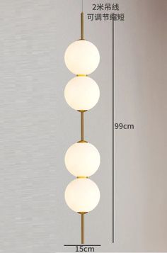 three white balls hanging from the ceiling in front of a wall with measurements on it