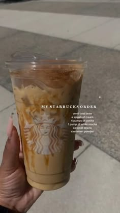 a person holding up a cup of coffee on the sidewalk with an advertisement above it