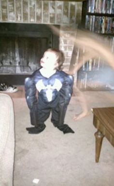 a young boy in a spiderman costume standing on the floor with his legs spread out