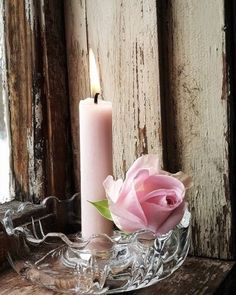 a pink rose sitting on top of a glass bowl next to a candle