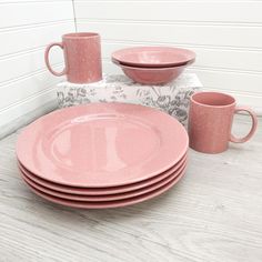 a stack of pink dishes sitting on top of a table next to cups and saucers