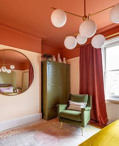 a green chair sitting in front of a mirror on top of a wooden dresser next to a window