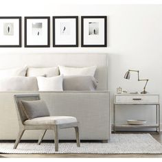 a white bed sitting next to two framed pictures on the wall in a room with a chair