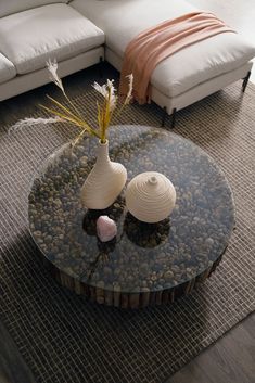 two white vases sitting on top of a glass table in front of a couch