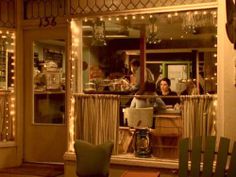 two people sitting at a table in front of a store window with lights on the windows