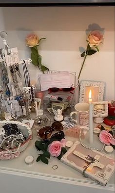 a table topped with lots of jewelry and flowers next to a candle on top of a table