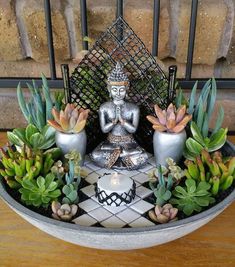 a buddha statue surrounded by succulents in a bowl on top of a table