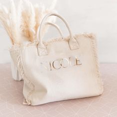 a white bag with the word nicole on it sitting next to a feathery plant