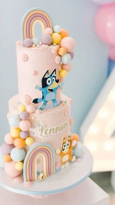 a three tiered cake decorated with cartoon characters and rainbows on the top layer