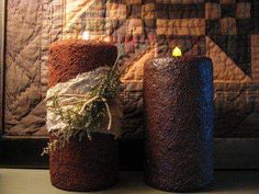 two candles are sitting on a table next to a quilted wall hanging with twine