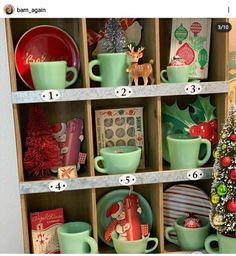 a shelf filled with green cups and saucers next to a christmas tree in a wooden box