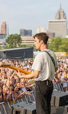 a man holding a guitar while standing in front of a large crowd at a concert